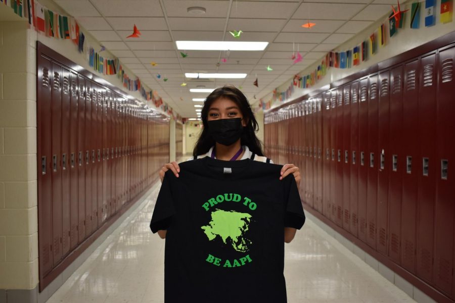 PROUD TO BE AAPI: Megan Wikowsky (12) is a part of the planning committee for Asian American Pacific Islander month in May and made t-shirts for students and staff to wear to support. She stands behind origami made by Audrey Lee (10)  hung in the ceiling tiles. 