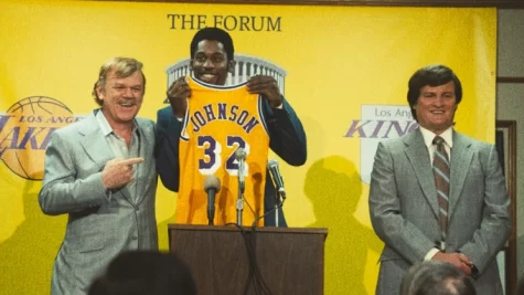Left to right Jerry Buss (John C. Reilly) presents a jersey to newly drafted Magic Johnson (Quincy Isaiah) alongside GM Jerry West (Jason Clarke)