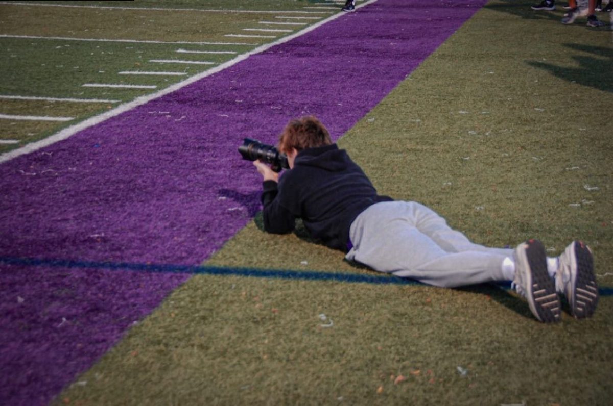 GETTING THE ANGLES RIGHT: Photographer Steven Toth (12) lays on the ground while taking pictures at a football game against Proviso West Sept. 15.